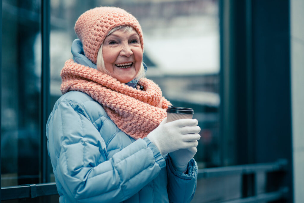 Mulher idosa soridente com roupas de inverno ao ar livre em um dia frio enquanto segura uma xícara de café